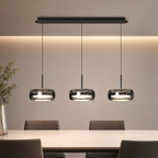 Glass drum pendant light glowing warm white above a dining table