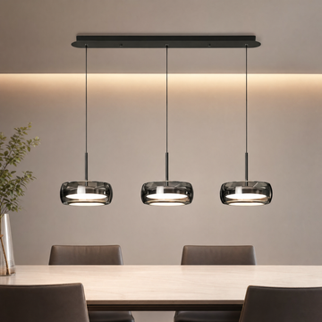 Glass drum pendant light glowing warm white above a dining table