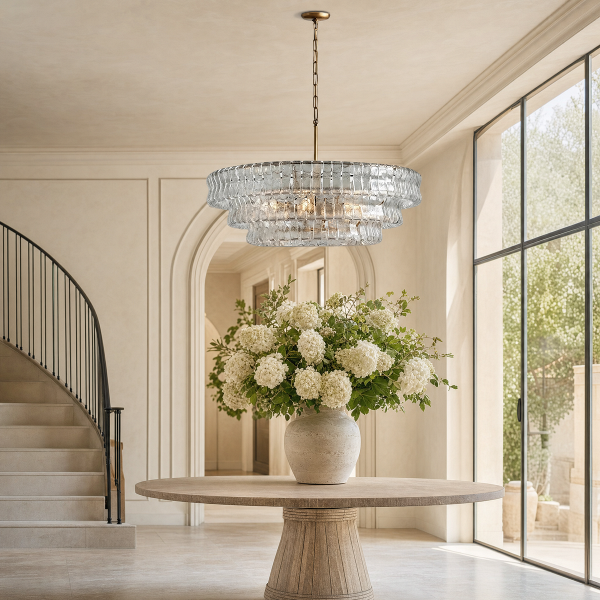 Ghiaccio glass round chandelier suspended in a bright entry foyer with curved staircase and floral centerpiece