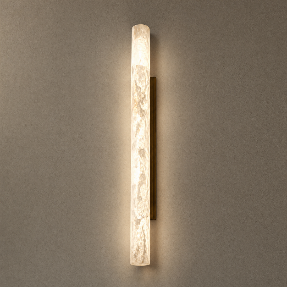 Alabaster pillar sconce glowing on a warm plaster wall with antique brass back plate