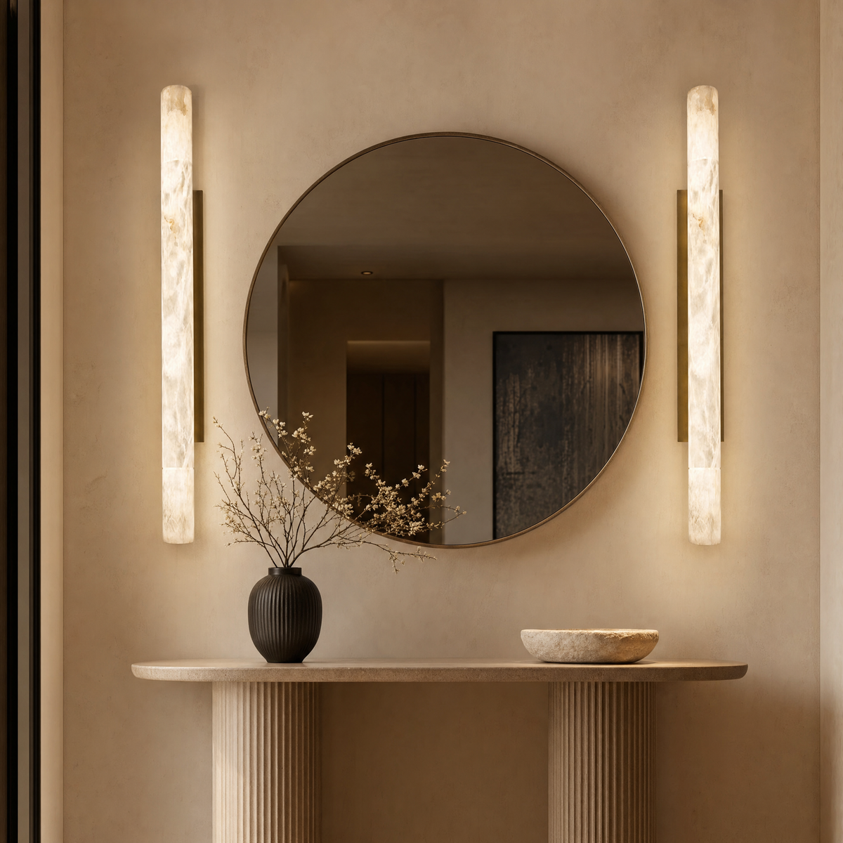 Pair of alabaster pillar sconces flanking a round mirror above a console in an entry hallway