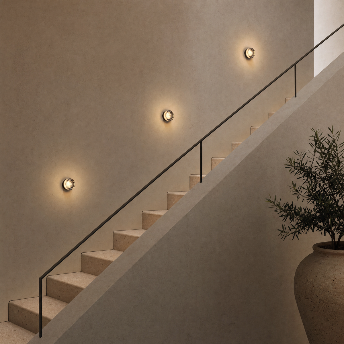 Three compact Vela wall sconces in Smoke Wave following the diagonal of a staircase wall at realistic install height